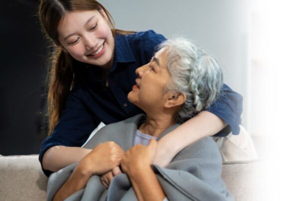 An adult child hugs an aging mother from behind her, wondering when it is time for assisted living.